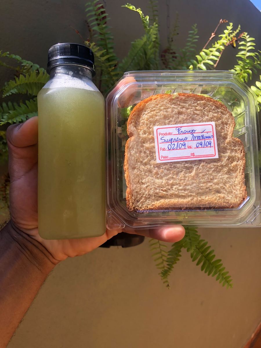 Mão segurando suco natural e lanche embalado